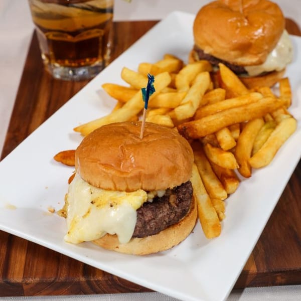 Two Prime 7 sliders with melted cheese and a side of golden fries, next to a drink.