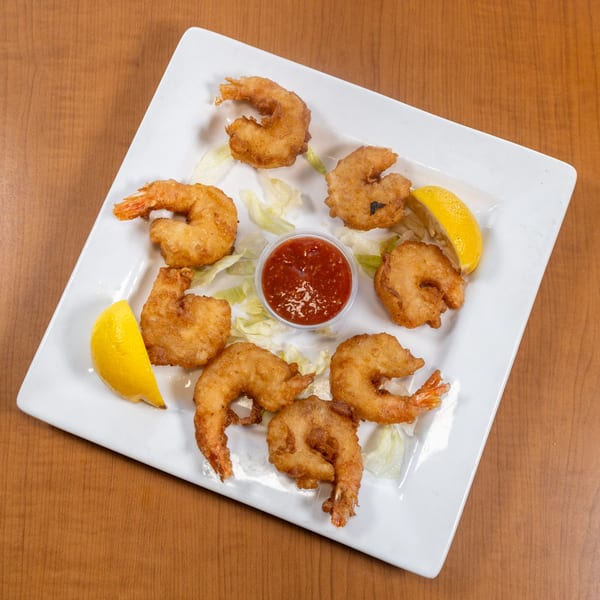 Plate of golden-fried shrimp with cocktail sauce, lemon wedges, and lettuce on a wooden table.